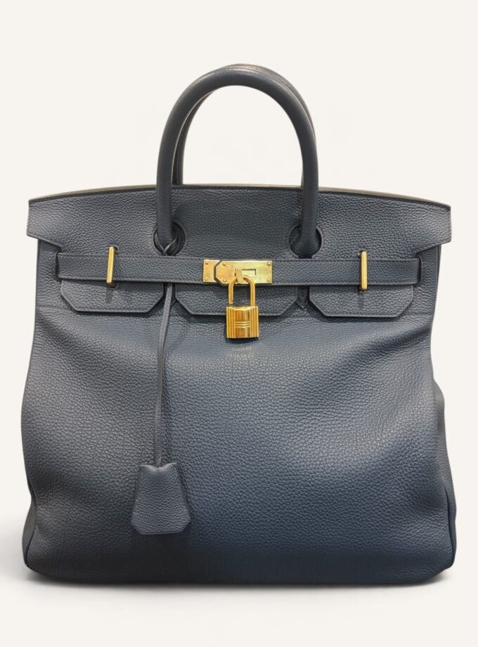 # Hermès HAC 40 Bleu de Prusse en cuir Togo, finitions Gold – 2015 Ce **HAC 40 Bleu de Prusse** en cuir Togo date de **2015**. Il se distingue par son magnifique bleu profond, associé à des **finitions Gold** qui apportent un contraste chaleureux. Présenté en **très bon état général**, cet exemplaire possède uniquement de légères traces d'utilisation au niveau des coins. Son format 40 et sa silhouette caractéristique lui confèrent une présence remarquable. **Dimensions : format 40 cm – dimensions complètes à compléter** **Matière : cuir Togo** **Couleur : Bleu de Prusse** **Finitions : Gold** **Année : 2015** **État : très bon état général, légères traces aux coins** Cette configuration associe l'élégance d'une couleur profonde à la texture du cuir Togo. Ainsi, le sac conserve une esthétique intemporelle tout en se distinguant des coloris plus traditionnels. --- ## HAC 40 Bleu de Prusse : une couleur profonde et élégante Le **Bleu de Prusse** fait partie des tonalités sombres particulièrement intéressantes de la palette Hermès. Sa profondeur lui donne une élégance proche de celle d'un bleu nuit. Cependant, ses nuances peuvent évoluer selon la lumière. Sous un éclairage naturel, le cuir peut révéler davantage de bleu. En revanche, dans une ambiance plus sombre, sa couleur apparaît plus intense. Cette richesse visuelle apporte une personnalité particulière au sac. De plus, le Bleu de Prusse s'associe facilement au noir, au gris, au beige et aux tons naturels. Il constitue donc une belle alternative aux grands sacs Hermès noirs ou marron. ## Le cuir Togo : une matière emblématique Le **cuir Togo** est apprécié pour son grain visible et son toucher souple. Il offre un équilibre intéressant entre structure et souplesse. Sur un grand format comme le HAC 40, cette matière permet de mettre en valeur les volumes du sac. Par ailleurs, sa surface grainée rend généralement les petites marques moins apparentes que sur certains cuirs lisses. Le résultat est un sac agréable à utiliser, tout en conservant une belle présence. Associé au Bleu de Prusse, le Togo révèle également de subtils jeux de lumière. ## Des finitions Gold au contraste raffiné Les **finitions Gold** jouent un rôle essentiel dans l'esthétique de cet exemplaire. Leur tonalité dorée contraste avec le bleu profond du cuir. Ainsi, les éléments métalliques deviennent de véritables détails décoratifs. Cette association apporte davantage de chaleur qu'une configuration accompagnée de finitions Palladium. De plus, le contraste entre le bleu et l'or renforce le caractère sophistiqué de ce HAC 40. Il s'agit d'une combinaison particulièrement élégante pour un grand sac de maroquinerie. ## Hermès HAC 40 : une silhouette historique Le **HAC**, ou *Haut à Courroies*, occupe une place particulière dans l'histoire d'Hermès. Créé à la fin du XIXe siècle, il était initialement destiné au transport des équipements équestres. Son nom fait référence à sa silhouette haute et à son système de fermeture à courroies. Au fil du temps, le modèle a évolué pour devenir une pièce emblématique de la maroquinerie de voyage Hermès. Aujourd'hui, il séduit aussi bien les collectionneurs que les amateurs de grands sacs de luxe. Son format généreux et sa structure reconnaissable lui donnent une identité distincte du Birkin. ## Un HAC 40 datant de 2015 Cet exemplaire a été fabriqué en **2015**. Il possède donc plus de dix années d'ancienneté. Malgré son âge, il est conservé dans un **très bon état général**. Seules de légères traces sont visibles au niveau des coins. Ces marques correspondent à une utilisation normale et restent limitées. Par ailleurs, elles sont clairement présentées afin de permettre une acquisition en toute transparence. ## Très bon état avec de légères traces aux coins L'état de conservation constitue un critère essentiel pour un sac Hermès d'occasion. Ce **HAC 40 Bleu de Prusse** est proposé en très bon état général. Le cuir Togo conserve une belle présentation. Cependant, quelques légères marques sont présentes aux coins. Ces zones sont naturellement exposées aux frottements lors de l'utilisation d'un sac. Nos photographies détaillées permettent donc d'apprécier précisément leur importance. Ainsi, l'acheteur dispose d'une description fidèle de l'état réel de la pièce. ## Le format HAC 40 : volume et élégance Le **format 40** offre un volume généreux. Il permet de transporter facilement de nombreux effets personnels. Ce sac peut notamment accueillir : - Un portefeuille. - Un téléphone. - Des lunettes. - Une pochette. - Des documents. - Une tablette. - Divers accessoires personnels. De plus, sa silhouette haute lui donne une présence plus affirmée que celle d'un sac à main classique. Il peut donc être envisagé comme un grand sac quotidien ou un élégant compagnon de déplacement. ## Un grand sac Hermès au caractère affirmé Le HAC 40 possède une esthétique immédiatement reconnaissable. Sa silhouette structurée et ses proportions généreuses lui confèrent une allure particulière. Sur cet exemplaire, le cuir Togo Bleu de Prusse apporte davantage de souplesse visuelle. En parallèle, les finitions Gold soulignent les lignes du sac. Ainsi, l'ensemble reste élégant malgré son volume important. Cette combinaison conviendra particulièrement aux amateurs de pièces Hermès discrètes par leur couleur, mais remarquables par leur format. ## Pourquoi choisir un HAC 40 Bleu de Prusse ? Cet exemplaire réunit plusieurs caractéristiques intéressantes : - **Modèle :** Hermès Haut à Courroies 40. - **Année :** 2015. - **Matière :** cuir Togo. - **Couleur :** Bleu de Prusse. - **Finitions :** Gold. - **État :** très bon état général. - **À noter :** légères traces d'utilisation aux coins. - **Format :** 40 cm. Cette configuration se distingue notamment par son équilibre entre couleur profonde, cuir grainé et finitions dorées. Elle constitue donc une belle option pour enrichir une collection Hermès ou acquérir un grand sac élégant. ## Une alternative aux HAC noirs et marron Les grands sacs Hermès sont souvent recherchés dans des couleurs classiques. Le noir, le Gold ou l'Ébène restent naturellement des choix intemporels. Toutefois, le Bleu de Prusse permet d'apporter davantage de personnalité sans choisir une couleur trop vive. Son intensité reste discrète. De plus, les finitions Gold créent un contraste qui souligne parfaitement le bleu du cuir. Ainsi, ce HAC 40 constitue une alternative particulièrement intéressante aux configurations traditionnelles. ## Un sac Hermès à porter et à conserver Grâce à son cuir Togo et à son format généreux, cet exemplaire peut être utilisé régulièrement. Il peut accompagner un vestiaire élégant ou plus décontracté. Cependant, sa couleur particulière lui donne également un intérêt pour les amateurs de configurations Hermès moins courantes. Le Bleu de Prusse permet notamment de varier une collection composée de sacs noirs, marron ou beiges. Ce HAC 40 peut donc aussi bien devenir un sac personnel qu'une belle pièce de collection. ## Pourquoi acheter votre HAC Hermès chez The Vintage Traveler ? Chez **The Vintage Traveler**, nous sélectionnons des sacs Hermès vintage et d'occasion pour leur authenticité, leur qualité et leurs caractéristiques. Chaque pièce est examinée avec attention afin de présenter précisément son état et ses particularités. ### Nos garanties ✔ **Magasin physique situé au Marché Paul Bert Serpette**, au cœur des Puces de Saint-Ouen. ✔ Sac **expertisé et certifié authentique** par un spécialiste du luxe vintage et d'occasion. ✔ Certificat d'authenticité fourni avec votre achat. ✔ Photographies détaillées et fidèles à l'état réel du sac. ✔ Description transparente des légères traces présentes aux coins. ✔ Accompagnement personnalisé avant et après votre achat. ✔ Expédition internationale rapide, sécurisée et assurée. --- ## Caractéristiques du Hermès HAC 40 **Maison :** Hermès **Modèle :** Haut à Courroies – HAC 40 **Année :** 2015 **Matière :** Cuir Togo **Couleur :** Bleu de Prusse **Finitions :** Gold **Format :** 40 cm **Dimensions complètes :** à compléter **État :** Très bon état général **À noter :** Légères traces d'utilisation aux coins --- ## Un élégant HAC 40 Bleu de Prusse de 2015 Ce **HAC 40 Bleu de Prusse** en cuir Togo constitue une superbe interprétation du célèbre Haut à Courroies Hermès. Sa couleur profonde, associée aux **finitions Gold**, lui donne une esthétique particulièrement raffinée. Datant de **2015**, cet exemplaire est conservé dans un **très bon état général**, avec seulement de légères traces aux coins. Enfin, son format 40 offre un volume généreux tout en conservant la silhouette emblématique du HAC. Une belle pièce pour les amateurs de **sacs Hermès d'occasion**, de grands formats et de couleurs sophistiquées.