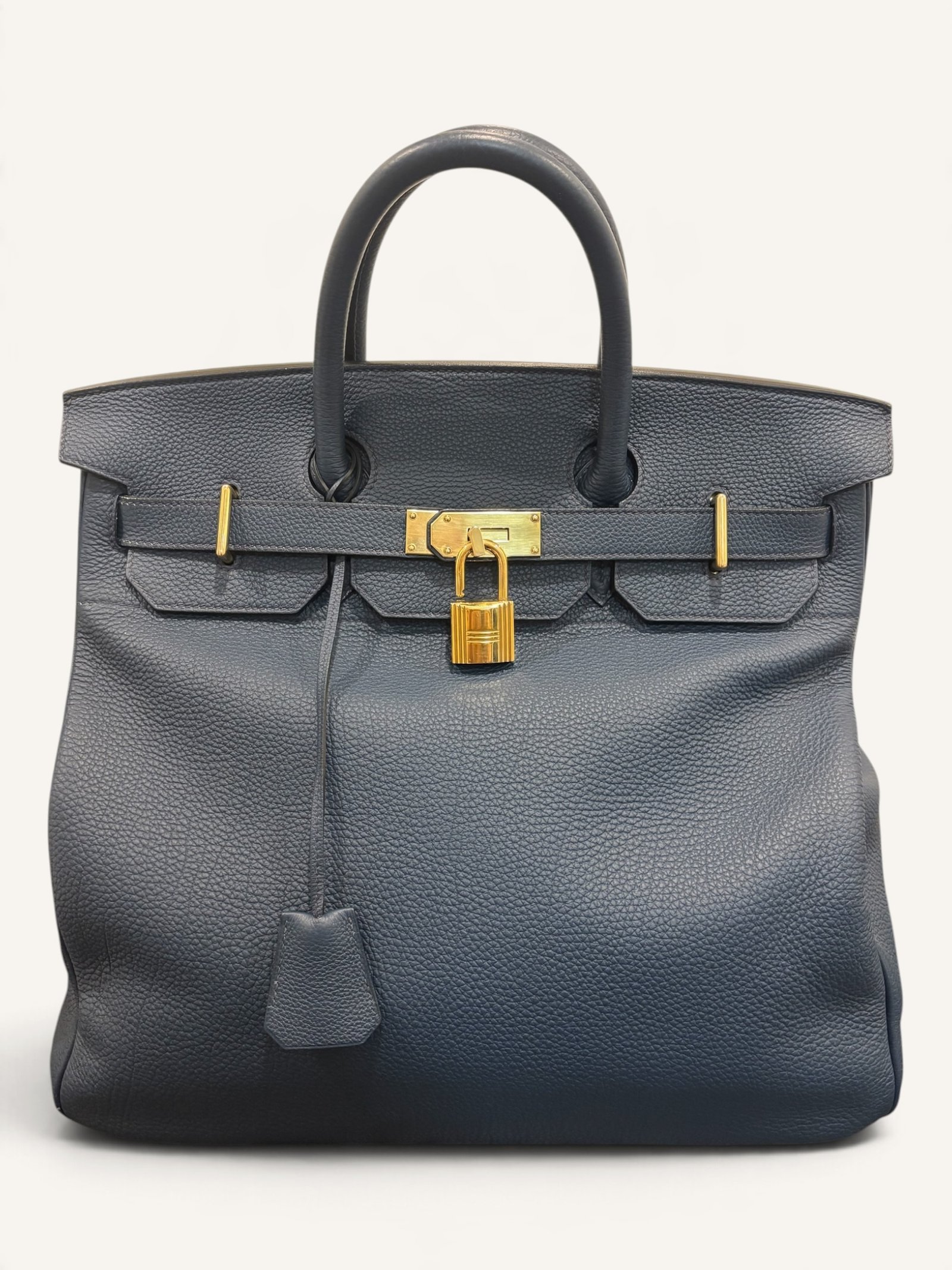 # Hermès HAC 40 Bleu de Prusse en cuir Togo, finitions Gold – 2015 Ce **HAC 40 Bleu de Prusse** en cuir Togo date de **2015**. Il se distingue par son magnifique bleu profond, associé à des **finitions Gold** qui apportent un contraste chaleureux. Présenté en **très bon état général**, cet exemplaire possède uniquement de légères traces d'utilisation au niveau des coins. Son format 40 et sa silhouette caractéristique lui confèrent une présence remarquable. **Dimensions : format 40 cm – dimensions complètes à compléter** **Matière : cuir Togo** **Couleur : Bleu de Prusse** **Finitions : Gold** **Année : 2015** **État : très bon état général, légères traces aux coins** Cette configuration associe l'élégance d'une couleur profonde à la texture du cuir Togo. Ainsi, le sac conserve une esthétique intemporelle tout en se distinguant des coloris plus traditionnels. --- ## HAC 40 Bleu de Prusse : une couleur profonde et élégante Le **Bleu de Prusse** fait partie des tonalités sombres particulièrement intéressantes de la palette Hermès. Sa profondeur lui donne une élégance proche de celle d'un bleu nuit. Cependant, ses nuances peuvent évoluer selon la lumière. Sous un éclairage naturel, le cuir peut révéler davantage de bleu. En revanche, dans une ambiance plus sombre, sa couleur apparaît plus intense. Cette richesse visuelle apporte une personnalité particulière au sac. De plus, le Bleu de Prusse s'associe facilement au noir, au gris, au beige et aux tons naturels. Il constitue donc une belle alternative aux grands sacs Hermès noirs ou marron. ## Le cuir Togo : une matière emblématique Le **cuir Togo** est apprécié pour son grain visible et son toucher souple. Il offre un équilibre intéressant entre structure et souplesse. Sur un grand format comme le HAC 40, cette matière permet de mettre en valeur les volumes du sac. Par ailleurs, sa surface grainée rend généralement les petites marques moins apparentes que sur certains cuirs lisses. Le résultat est un sac agréable à utiliser, tout en conservant une belle présence. Associé au Bleu de Prusse, le Togo révèle également de subtils jeux de lumière. ## Des finitions Gold au contraste raffiné Les **finitions Gold** jouent un rôle essentiel dans l'esthétique de cet exemplaire. Leur tonalité dorée contraste avec le bleu profond du cuir. Ainsi, les éléments métalliques deviennent de véritables détails décoratifs. Cette association apporte davantage de chaleur qu'une configuration accompagnée de finitions Palladium. De plus, le contraste entre le bleu et l'or renforce le caractère sophistiqué de ce HAC 40. Il s'agit d'une combinaison particulièrement élégante pour un grand sac de maroquinerie. ## Hermès HAC 40 : une silhouette historique Le **HAC**, ou *Haut à Courroies*, occupe une place particulière dans l'histoire d'Hermès. Créé à la fin du XIXe siècle, il était initialement destiné au transport des équipements équestres. Son nom fait référence à sa silhouette haute et à son système de fermeture à courroies. Au fil du temps, le modèle a évolué pour devenir une pièce emblématique de la maroquinerie de voyage Hermès. Aujourd'hui, il séduit aussi bien les collectionneurs que les amateurs de grands sacs de luxe. Son format généreux et sa structure reconnaissable lui donnent une identité distincte du Birkin. ## Un HAC 40 datant de 2015 Cet exemplaire a été fabriqué en **2015**. Il possède donc plus de dix années d'ancienneté. Malgré son âge, il est conservé dans un **très bon état général**. Seules de légères traces sont visibles au niveau des coins. Ces marques correspondent à une utilisation normale et restent limitées. Par ailleurs, elles sont clairement présentées afin de permettre une acquisition en toute transparence. ## Très bon état avec de légères traces aux coins L'état de conservation constitue un critère essentiel pour un sac Hermès d'occasion. Ce **HAC 40 Bleu de Prusse** est proposé en très bon état général. Le cuir Togo conserve une belle présentation. Cependant, quelques légères marques sont présentes aux coins. Ces zones sont naturellement exposées aux frottements lors de l'utilisation d'un sac. Nos photographies détaillées permettent donc d'apprécier précisément leur importance. Ainsi, l'acheteur dispose d'une description fidèle de l'état réel de la pièce. ## Le format HAC 40 : volume et élégance Le **format 40** offre un volume généreux. Il permet de transporter facilement de nombreux effets personnels. Ce sac peut notamment accueillir : - Un portefeuille. - Un téléphone. - Des lunettes. - Une pochette. - Des documents. - Une tablette. - Divers accessoires personnels. De plus, sa silhouette haute lui donne une présence plus affirmée que celle d'un sac à main classique. Il peut donc être envisagé comme un grand sac quotidien ou un élégant compagnon de déplacement. ## Un grand sac Hermès au caractère affirmé Le HAC 40 possède une esthétique immédiatement reconnaissable. Sa silhouette structurée et ses proportions généreuses lui confèrent une allure particulière. Sur cet exemplaire, le cuir Togo Bleu de Prusse apporte davantage de souplesse visuelle. En parallèle, les finitions Gold soulignent les lignes du sac. Ainsi, l'ensemble reste élégant malgré son volume important. Cette combinaison conviendra particulièrement aux amateurs de pièces Hermès discrètes par leur couleur, mais remarquables par leur format. ## Pourquoi choisir un HAC 40 Bleu de Prusse ? Cet exemplaire réunit plusieurs caractéristiques intéressantes : - **Modèle :** Hermès Haut à Courroies 40. - **Année :** 2015. - **Matière :** cuir Togo. - **Couleur :** Bleu de Prusse. - **Finitions :** Gold. - **État :** très bon état général. - **À noter :** légères traces d'utilisation aux coins. - **Format :** 40 cm. Cette configuration se distingue notamment par son équilibre entre couleur profonde, cuir grainé et finitions dorées. Elle constitue donc une belle option pour enrichir une collection Hermès ou acquérir un grand sac élégant. ## Une alternative aux HAC noirs et marron Les grands sacs Hermès sont souvent recherchés dans des couleurs classiques. Le noir, le Gold ou l'Ébène restent naturellement des choix intemporels. Toutefois, le Bleu de Prusse permet d'apporter davantage de personnalité sans choisir une couleur trop vive. Son intensité reste discrète. De plus, les finitions Gold créent un contraste qui souligne parfaitement le bleu du cuir. Ainsi, ce HAC 40 constitue une alternative particulièrement intéressante aux configurations traditionnelles. ## Un sac Hermès à porter et à conserver Grâce à son cuir Togo et à son format généreux, cet exemplaire peut être utilisé régulièrement. Il peut accompagner un vestiaire élégant ou plus décontracté. Cependant, sa couleur particulière lui donne également un intérêt pour les amateurs de configurations Hermès moins courantes. Le Bleu de Prusse permet notamment de varier une collection composée de sacs noirs, marron ou beiges. Ce HAC 40 peut donc aussi bien devenir un sac personnel qu'une belle pièce de collection. ## Pourquoi acheter votre HAC Hermès chez The Vintage Traveler ? Chez **The Vintage Traveler**, nous sélectionnons des sacs Hermès vintage et d'occasion pour leur authenticité, leur qualité et leurs caractéristiques. Chaque pièce est examinée avec attention afin de présenter précisément son état et ses particularités. ### Nos garanties ✔ **Magasin physique situé au Marché Paul Bert Serpette**, au cœur des Puces de Saint-Ouen. ✔ Sac **expertisé et certifié authentique** par un spécialiste du luxe vintage et d'occasion. ✔ Certificat d'authenticité fourni avec votre achat. ✔ Photographies détaillées et fidèles à l'état réel du sac. ✔ Description transparente des légères traces présentes aux coins. ✔ Accompagnement personnalisé avant et après votre achat. ✔ Expédition internationale rapide, sécurisée et assurée. --- ## Caractéristiques du Hermès HAC 40 **Maison :** Hermès **Modèle :** Haut à Courroies – HAC 40 **Année :** 2015 **Matière :** Cuir Togo **Couleur :** Bleu de Prusse **Finitions :** Gold **Format :** 40 cm **Dimensions complètes :** à compléter **État :** Très bon état général **À noter :** Légères traces d'utilisation aux coins --- ## Un élégant HAC 40 Bleu de Prusse de 2015 Ce **HAC 40 Bleu de Prusse** en cuir Togo constitue une superbe interprétation du célèbre Haut à Courroies Hermès. Sa couleur profonde, associée aux **finitions Gold**, lui donne une esthétique particulièrement raffinée. Datant de **2015**, cet exemplaire est conservé dans un **très bon état général**, avec seulement de légères traces aux coins. Enfin, son format 40 offre un volume généreux tout en conservant la silhouette emblématique du HAC. Une belle pièce pour les amateurs de **sacs Hermès d'occasion**, de grands formats et de couleurs sophistiquées.