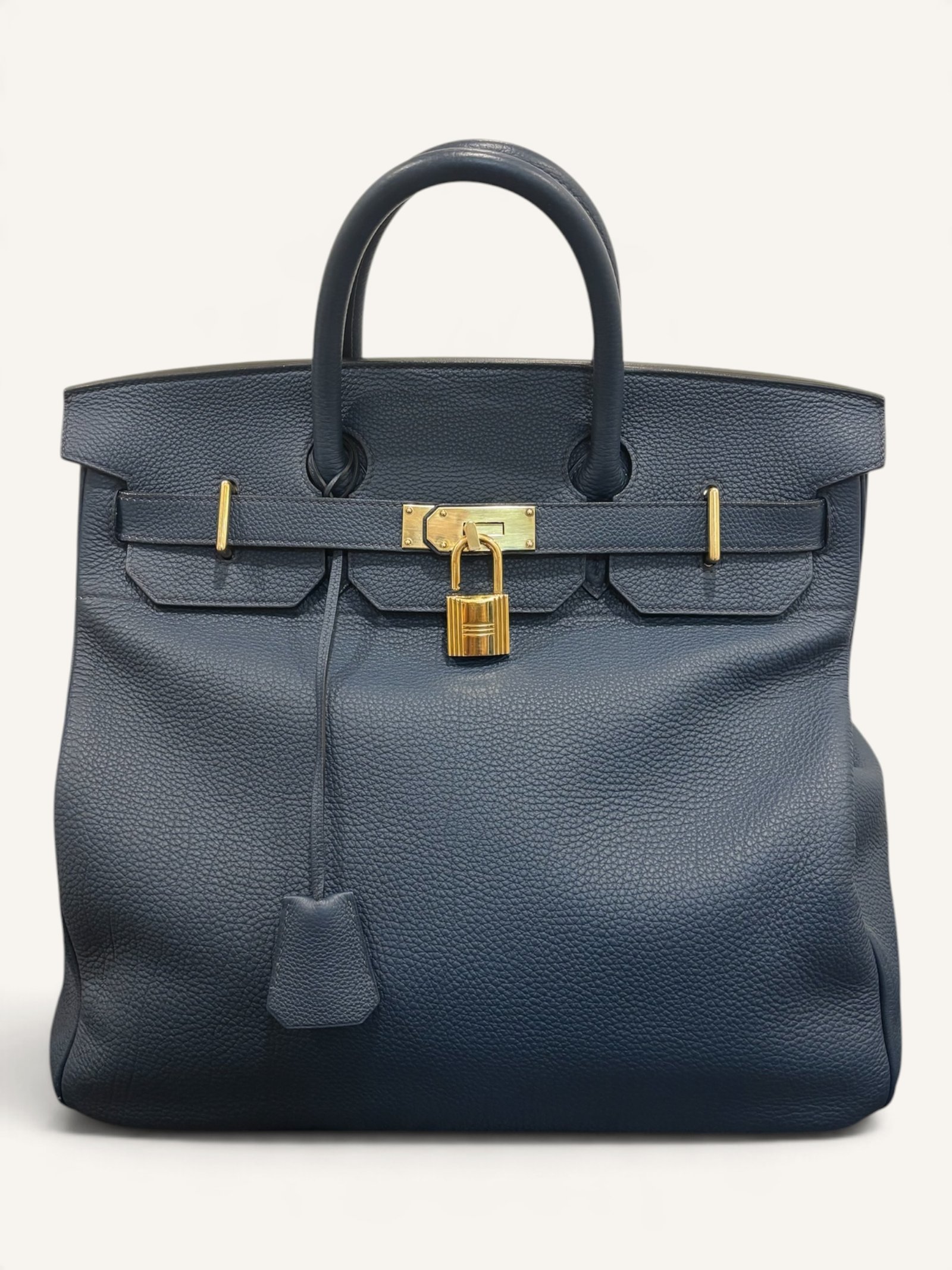 # Hermès HAC 40 Bleu de Prusse en cuir Togo, finitions Gold – 2015 Ce **HAC 40 Bleu de Prusse** en cuir Togo date de **2015**. Il se distingue par son magnifique bleu profond, associé à des **finitions Gold** qui apportent un contraste chaleureux. Présenté en **très bon état général**, cet exemplaire possède uniquement de légères traces d'utilisation au niveau des coins. Son format 40 et sa silhouette caractéristique lui confèrent une présence remarquable. **Dimensions : format 40 cm – dimensions complètes à compléter** **Matière : cuir Togo** **Couleur : Bleu de Prusse** **Finitions : Gold** **Année : 2015** **État : très bon état général, légères traces aux coins** Cette configuration associe l'élégance d'une couleur profonde à la texture du cuir Togo. Ainsi, le sac conserve une esthétique intemporelle tout en se distinguant des coloris plus traditionnels. --- ## HAC 40 Bleu de Prusse : une couleur profonde et élégante Le **Bleu de Prusse** fait partie des tonalités sombres particulièrement intéressantes de la palette Hermès. Sa profondeur lui donne une élégance proche de celle d'un bleu nuit. Cependant, ses nuances peuvent évoluer selon la lumière. Sous un éclairage naturel, le cuir peut révéler davantage de bleu. En revanche, dans une ambiance plus sombre, sa couleur apparaît plus intense. Cette richesse visuelle apporte une personnalité particulière au sac. De plus, le Bleu de Prusse s'associe facilement au noir, au gris, au beige et aux tons naturels. Il constitue donc une belle alternative aux grands sacs Hermès noirs ou marron. ## Le cuir Togo : une matière emblématique Le **cuir Togo** est apprécié pour son grain visible et son toucher souple. Il offre un équilibre intéressant entre structure et souplesse. Sur un grand format comme le HAC 40, cette matière permet de mettre en valeur les volumes du sac. Par ailleurs, sa surface grainée rend généralement les petites marques moins apparentes que sur certains cuirs lisses. Le résultat est un sac agréable à utiliser, tout en conservant une belle présence. Associé au Bleu de Prusse, le Togo révèle également de subtils jeux de lumière. ## Des finitions Gold au contraste raffiné Les **finitions Gold** jouent un rôle essentiel dans l'esthétique de cet exemplaire. Leur tonalité dorée contraste avec le bleu profond du cuir. Ainsi, les éléments métalliques deviennent de véritables détails décoratifs. Cette association apporte davantage de chaleur qu'une configuration accompagnée de finitions Palladium. De plus, le contraste entre le bleu et l'or renforce le caractère sophistiqué de ce HAC 40. Il s'agit d'une combinaison particulièrement élégante pour un grand sac de maroquinerie. ## Hermès HAC 40 : une silhouette historique Le **HAC**, ou *Haut à Courroies*, occupe une place particulière dans l'histoire d'Hermès. Créé à la fin du XIXe siècle, il était initialement destiné au transport des équipements équestres. Son nom fait référence à sa silhouette haute et à son système de fermeture à courroies. Au fil du temps, le modèle a évolué pour devenir une pièce emblématique de la maroquinerie de voyage Hermès. Aujourd'hui, il séduit aussi bien les collectionneurs que les amateurs de grands sacs de luxe. Son format généreux et sa structure reconnaissable lui donnent une identité distincte du Birkin. ## Un HAC 40 datant de 2015 Cet exemplaire a été fabriqué en **2015**. Il possède donc plus de dix années d'ancienneté. Malgré son âge, il est conservé dans un **très bon état général**. Seules de légères traces sont visibles au niveau des coins. Ces marques correspondent à une utilisation normale et restent limitées. Par ailleurs, elles sont clairement présentées afin de permettre une acquisition en toute transparence. ## Très bon état avec de légères traces aux coins L'état de conservation constitue un critère essentiel pour un sac Hermès d'occasion. Ce **HAC 40 Bleu de Prusse** est proposé en très bon état général. Le cuir Togo conserve une belle présentation. Cependant, quelques légères marques sont présentes aux coins. Ces zones sont naturellement exposées aux frottements lors de l'utilisation d'un sac. Nos photographies détaillées permettent donc d'apprécier précisément leur importance. Ainsi, l'acheteur dispose d'une description fidèle de l'état réel de la pièce. ## Le format HAC 40 : volume et élégance Le **format 40** offre un volume généreux. Il permet de transporter facilement de nombreux effets personnels. Ce sac peut notamment accueillir : - Un portefeuille. - Un téléphone. - Des lunettes. - Une pochette. - Des documents. - Une tablette. - Divers accessoires personnels. De plus, sa silhouette haute lui donne une présence plus affirmée que celle d'un sac à main classique. Il peut donc être envisagé comme un grand sac quotidien ou un élégant compagnon de déplacement. ## Un grand sac Hermès au caractère affirmé Le HAC 40 possède une esthétique immédiatement reconnaissable. Sa silhouette structurée et ses proportions généreuses lui confèrent une allure particulière. Sur cet exemplaire, le cuir Togo Bleu de Prusse apporte davantage de souplesse visuelle. En parallèle, les finitions Gold soulignent les lignes du sac. Ainsi, l'ensemble reste élégant malgré son volume important. Cette combinaison conviendra particulièrement aux amateurs de pièces Hermès discrètes par leur couleur, mais remarquables par leur format. ## Pourquoi choisir un HAC 40 Bleu de Prusse ? Cet exemplaire réunit plusieurs caractéristiques intéressantes : - **Modèle :** Hermès Haut à Courroies 40. - **Année :** 2015. - **Matière :** cuir Togo. - **Couleur :** Bleu de Prusse. - **Finitions :** Gold. - **État :** très bon état général. - **À noter :** légères traces d'utilisation aux coins. - **Format :** 40 cm. Cette configuration se distingue notamment par son équilibre entre couleur profonde, cuir grainé et finitions dorées. Elle constitue donc une belle option pour enrichir une collection Hermès ou acquérir un grand sac élégant. ## Une alternative aux HAC noirs et marron Les grands sacs Hermès sont souvent recherchés dans des couleurs classiques. Le noir, le Gold ou l'Ébène restent naturellement des choix intemporels. Toutefois, le Bleu de Prusse permet d'apporter davantage de personnalité sans choisir une couleur trop vive. Son intensité reste discrète. De plus, les finitions Gold créent un contraste qui souligne parfaitement le bleu du cuir. Ainsi, ce HAC 40 constitue une alternative particulièrement intéressante aux configurations traditionnelles. ## Un sac Hermès à porter et à conserver Grâce à son cuir Togo et à son format généreux, cet exemplaire peut être utilisé régulièrement. Il peut accompagner un vestiaire élégant ou plus décontracté. Cependant, sa couleur particulière lui donne également un intérêt pour les amateurs de configurations Hermès moins courantes. Le Bleu de Prusse permet notamment de varier une collection composée de sacs noirs, marron ou beiges. Ce HAC 40 peut donc aussi bien devenir un sac personnel qu'une belle pièce de collection. ## Pourquoi acheter votre HAC Hermès chez The Vintage Traveler ? Chez **The Vintage Traveler**, nous sélectionnons des sacs Hermès vintage et d'occasion pour leur authenticité, leur qualité et leurs caractéristiques. Chaque pièce est examinée avec attention afin de présenter précisément son état et ses particularités. ### Nos garanties ✔ **Magasin physique situé au Marché Paul Bert Serpette**, au cœur des Puces de Saint-Ouen. ✔ Sac **expertisé et certifié authentique** par un spécialiste du luxe vintage et d'occasion. ✔ Certificat d'authenticité fourni avec votre achat. ✔ Photographies détaillées et fidèles à l'état réel du sac. ✔ Description transparente des légères traces présentes aux coins. ✔ Accompagnement personnalisé avant et après votre achat. ✔ Expédition internationale rapide, sécurisée et assurée. --- ## Caractéristiques du Hermès HAC 40 **Maison :** Hermès **Modèle :** Haut à Courroies – HAC 40 **Année :** 2015 **Matière :** Cuir Togo **Couleur :** Bleu de Prusse **Finitions :** Gold **Format :** 40 cm **Dimensions complètes :** à compléter **État :** Très bon état général **À noter :** Légères traces d'utilisation aux coins --- ## Un élégant HAC 40 Bleu de Prusse de 2015 Ce **HAC 40 Bleu de Prusse** en cuir Togo constitue une superbe interprétation du célèbre Haut à Courroies Hermès. Sa couleur profonde, associée aux **finitions Gold**, lui donne une esthétique particulièrement raffinée. Datant de **2015**, cet exemplaire est conservé dans un **très bon état général**, avec seulement de légères traces aux coins. Enfin, son format 40 offre un volume généreux tout en conservant la silhouette emblématique du HAC. Une belle pièce pour les amateurs de **sacs Hermès d'occasion**, de grands formats et de couleurs sophistiquées.