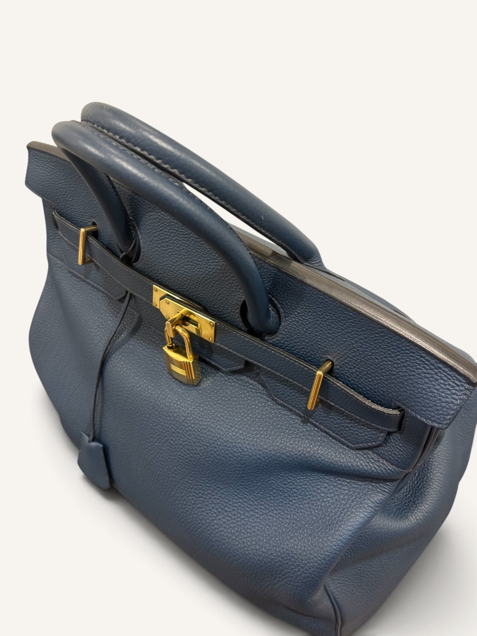 # Hermès HAC 40 Bleu de Prusse en cuir Togo, finitions Gold – 2015 Ce **HAC 40 Bleu de Prusse** en cuir Togo date de **2015**. Il se distingue par son magnifique bleu profond, associé à des **finitions Gold** qui apportent un contraste chaleureux. Présenté en **très bon état général**, cet exemplaire possède uniquement de légères traces d'utilisation au niveau des coins. Son format 40 et sa silhouette caractéristique lui confèrent une présence remarquable. **Dimensions : format 40 cm – dimensions complètes à compléter** **Matière : cuir Togo** **Couleur : Bleu de Prusse** **Finitions : Gold** **Année : 2015** **État : très bon état général, légères traces aux coins** Cette configuration associe l'élégance d'une couleur profonde à la texture du cuir Togo. Ainsi, le sac conserve une esthétique intemporelle tout en se distinguant des coloris plus traditionnels. --- ## HAC 40 Bleu de Prusse : une couleur profonde et élégante Le **Bleu de Prusse** fait partie des tonalités sombres particulièrement intéressantes de la palette Hermès. Sa profondeur lui donne une élégance proche de celle d'un bleu nuit. Cependant, ses nuances peuvent évoluer selon la lumière. Sous un éclairage naturel, le cuir peut révéler davantage de bleu. En revanche, dans une ambiance plus sombre, sa couleur apparaît plus intense. Cette richesse visuelle apporte une personnalité particulière au sac. De plus, le Bleu de Prusse s'associe facilement au noir, au gris, au beige et aux tons naturels. Il constitue donc une belle alternative aux grands sacs Hermès noirs ou marron. ## Le cuir Togo : une matière emblématique Le **cuir Togo** est apprécié pour son grain visible et son toucher souple. Il offre un équilibre intéressant entre structure et souplesse. Sur un grand format comme le HAC 40, cette matière permet de mettre en valeur les volumes du sac. Par ailleurs, sa surface grainée rend généralement les petites marques moins apparentes que sur certains cuirs lisses. Le résultat est un sac agréable à utiliser, tout en conservant une belle présence. Associé au Bleu de Prusse, le Togo révèle également de subtils jeux de lumière. ## Des finitions Gold au contraste raffiné Les **finitions Gold** jouent un rôle essentiel dans l'esthétique de cet exemplaire. Leur tonalité dorée contraste avec le bleu profond du cuir. Ainsi, les éléments métalliques deviennent de véritables détails décoratifs. Cette association apporte davantage de chaleur qu'une configuration accompagnée de finitions Palladium. De plus, le contraste entre le bleu et l'or renforce le caractère sophistiqué de ce HAC 40. Il s'agit d'une combinaison particulièrement élégante pour un grand sac de maroquinerie. ## Hermès HAC 40 : une silhouette historique Le **HAC**, ou *Haut à Courroies*, occupe une place particulière dans l'histoire d'Hermès. Créé à la fin du XIXe siècle, il était initialement destiné au transport des équipements équestres. Son nom fait référence à sa silhouette haute et à son système de fermeture à courroies. Au fil du temps, le modèle a évolué pour devenir une pièce emblématique de la maroquinerie de voyage Hermès. Aujourd'hui, il séduit aussi bien les collectionneurs que les amateurs de grands sacs de luxe. Son format généreux et sa structure reconnaissable lui donnent une identité distincte du Birkin. ## Un HAC 40 datant de 2015 Cet exemplaire a été fabriqué en **2015**. Il possède donc plus de dix années d'ancienneté. Malgré son âge, il est conservé dans un **très bon état général**. Seules de légères traces sont visibles au niveau des coins. Ces marques correspondent à une utilisation normale et restent limitées. Par ailleurs, elles sont clairement présentées afin de permettre une acquisition en toute transparence. ## Très bon état avec de légères traces aux coins L'état de conservation constitue un critère essentiel pour un sac Hermès d'occasion. Ce **HAC 40 Bleu de Prusse** est proposé en très bon état général. Le cuir Togo conserve une belle présentation. Cependant, quelques légères marques sont présentes aux coins. Ces zones sont naturellement exposées aux frottements lors de l'utilisation d'un sac. Nos photographies détaillées permettent donc d'apprécier précisément leur importance. Ainsi, l'acheteur dispose d'une description fidèle de l'état réel de la pièce. ## Le format HAC 40 : volume et élégance Le **format 40** offre un volume généreux. Il permet de transporter facilement de nombreux effets personnels. Ce sac peut notamment accueillir : - Un portefeuille. - Un téléphone. - Des lunettes. - Une pochette. - Des documents. - Une tablette. - Divers accessoires personnels. De plus, sa silhouette haute lui donne une présence plus affirmée que celle d'un sac à main classique. Il peut donc être envisagé comme un grand sac quotidien ou un élégant compagnon de déplacement. ## Un grand sac Hermès au caractère affirmé Le HAC 40 possède une esthétique immédiatement reconnaissable. Sa silhouette structurée et ses proportions généreuses lui confèrent une allure particulière. Sur cet exemplaire, le cuir Togo Bleu de Prusse apporte davantage de souplesse visuelle. En parallèle, les finitions Gold soulignent les lignes du sac. Ainsi, l'ensemble reste élégant malgré son volume important. Cette combinaison conviendra particulièrement aux amateurs de pièces Hermès discrètes par leur couleur, mais remarquables par leur format. ## Pourquoi choisir un HAC 40 Bleu de Prusse ? Cet exemplaire réunit plusieurs caractéristiques intéressantes : - **Modèle :** Hermès Haut à Courroies 40. - **Année :** 2015. - **Matière :** cuir Togo. - **Couleur :** Bleu de Prusse. - **Finitions :** Gold. - **État :** très bon état général. - **À noter :** légères traces d'utilisation aux coins. - **Format :** 40 cm. Cette configuration se distingue notamment par son équilibre entre couleur profonde, cuir grainé et finitions dorées. Elle constitue donc une belle option pour enrichir une collection Hermès ou acquérir un grand sac élégant. ## Une alternative aux HAC noirs et marron Les grands sacs Hermès sont souvent recherchés dans des couleurs classiques. Le noir, le Gold ou l'Ébène restent naturellement des choix intemporels. Toutefois, le Bleu de Prusse permet d'apporter davantage de personnalité sans choisir une couleur trop vive. Son intensité reste discrète. De plus, les finitions Gold créent un contraste qui souligne parfaitement le bleu du cuir. Ainsi, ce HAC 40 constitue une alternative particulièrement intéressante aux configurations traditionnelles. ## Un sac Hermès à porter et à conserver Grâce à son cuir Togo et à son format généreux, cet exemplaire peut être utilisé régulièrement. Il peut accompagner un vestiaire élégant ou plus décontracté. Cependant, sa couleur particulière lui donne également un intérêt pour les amateurs de configurations Hermès moins courantes. Le Bleu de Prusse permet notamment de varier une collection composée de sacs noirs, marron ou beiges. Ce HAC 40 peut donc aussi bien devenir un sac personnel qu'une belle pièce de collection. ## Pourquoi acheter votre HAC Hermès chez The Vintage Traveler ? Chez **The Vintage Traveler**, nous sélectionnons des sacs Hermès vintage et d'occasion pour leur authenticité, leur qualité et leurs caractéristiques. Chaque pièce est examinée avec attention afin de présenter précisément son état et ses particularités. ### Nos garanties ✔ **Magasin physique situé au Marché Paul Bert Serpette**, au cœur des Puces de Saint-Ouen. ✔ Sac **expertisé et certifié authentique** par un spécialiste du luxe vintage et d'occasion. ✔ Certificat d'authenticité fourni avec votre achat. ✔ Photographies détaillées et fidèles à l'état réel du sac. ✔ Description transparente des légères traces présentes aux coins. ✔ Accompagnement personnalisé avant et après votre achat. ✔ Expédition internationale rapide, sécurisée et assurée. --- ## Caractéristiques du Hermès HAC 40 **Maison :** Hermès **Modèle :** Haut à Courroies – HAC 40 **Année :** 2015 **Matière :** Cuir Togo **Couleur :** Bleu de Prusse **Finitions :** Gold **Format :** 40 cm **Dimensions complètes :** à compléter **État :** Très bon état général **À noter :** Légères traces d'utilisation aux coins --- ## Un élégant HAC 40 Bleu de Prusse de 2015 Ce **HAC 40 Bleu de Prusse** en cuir Togo constitue une superbe interprétation du célèbre Haut à Courroies Hermès. Sa couleur profonde, associée aux **finitions Gold**, lui donne une esthétique particulièrement raffinée. Datant de **2015**, cet exemplaire est conservé dans un **très bon état général**, avec seulement de légères traces aux coins. Enfin, son format 40 offre un volume généreux tout en conservant la silhouette emblématique du HAC. Une belle pièce pour les amateurs de **sacs Hermès d'occasion**, de grands formats et de couleurs sophistiquées.