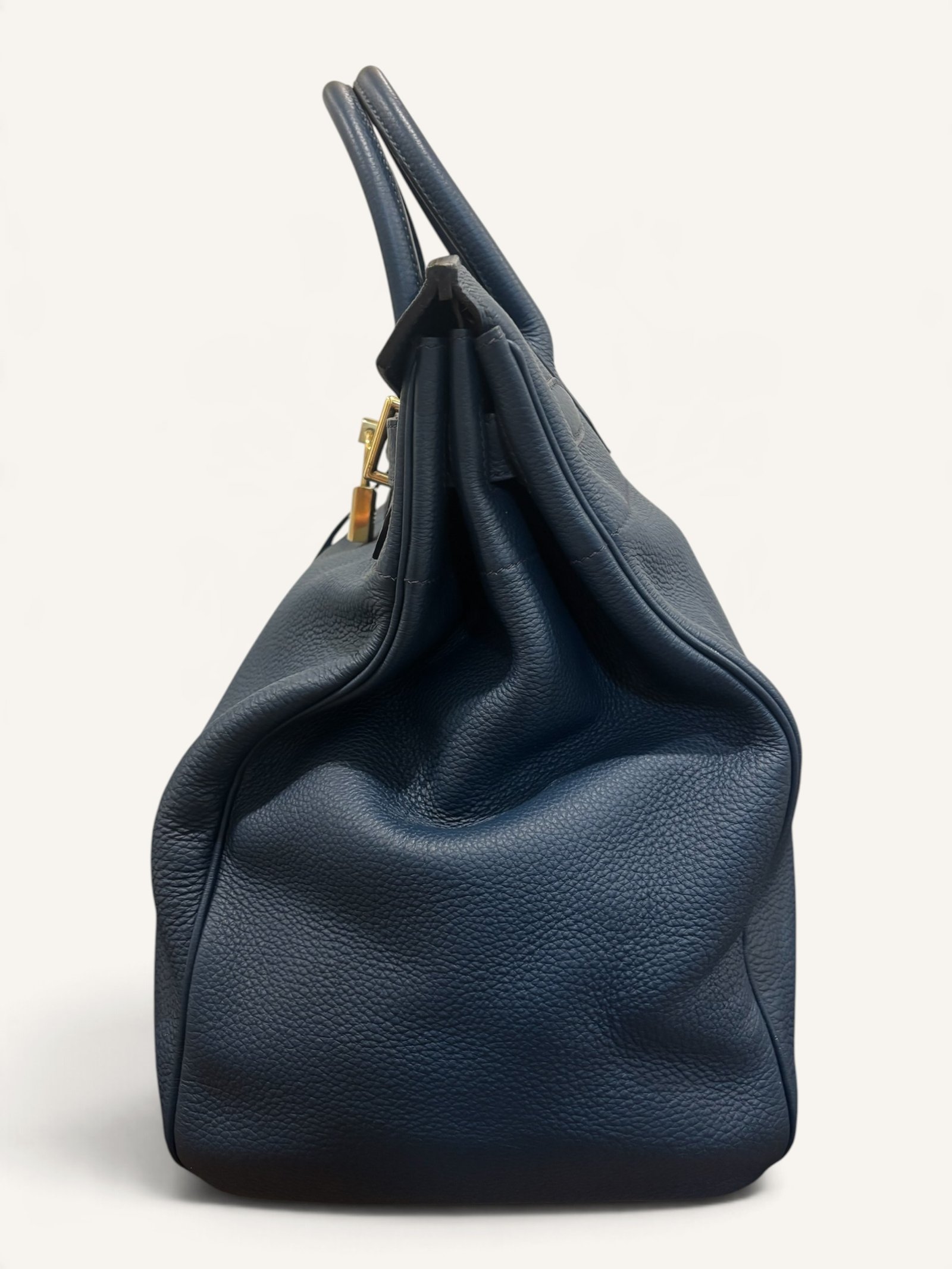 # Hermès HAC 40 Bleu de Prusse en cuir Togo, finitions Gold – 2015 Ce **HAC 40 Bleu de Prusse** en cuir Togo date de **2015**. Il se distingue par son magnifique bleu profond, associé à des **finitions Gold** qui apportent un contraste chaleureux. Présenté en **très bon état général**, cet exemplaire possède uniquement de légères traces d'utilisation au niveau des coins. Son format 40 et sa silhouette caractéristique lui confèrent une présence remarquable. **Dimensions : format 40 cm – dimensions complètes à compléter** **Matière : cuir Togo** **Couleur : Bleu de Prusse** **Finitions : Gold** **Année : 2015** **État : très bon état général, légères traces aux coins** Cette configuration associe l'élégance d'une couleur profonde à la texture du cuir Togo. Ainsi, le sac conserve une esthétique intemporelle tout en se distinguant des coloris plus traditionnels. --- ## HAC 40 Bleu de Prusse : une couleur profonde et élégante Le **Bleu de Prusse** fait partie des tonalités sombres particulièrement intéressantes de la palette Hermès. Sa profondeur lui donne une élégance proche de celle d'un bleu nuit. Cependant, ses nuances peuvent évoluer selon la lumière. Sous un éclairage naturel, le cuir peut révéler davantage de bleu. En revanche, dans une ambiance plus sombre, sa couleur apparaît plus intense. Cette richesse visuelle apporte une personnalité particulière au sac. De plus, le Bleu de Prusse s'associe facilement au noir, au gris, au beige et aux tons naturels. Il constitue donc une belle alternative aux grands sacs Hermès noirs ou marron. ## Le cuir Togo : une matière emblématique Le **cuir Togo** est apprécié pour son grain visible et son toucher souple. Il offre un équilibre intéressant entre structure et souplesse. Sur un grand format comme le HAC 40, cette matière permet de mettre en valeur les volumes du sac. Par ailleurs, sa surface grainée rend généralement les petites marques moins apparentes que sur certains cuirs lisses. Le résultat est un sac agréable à utiliser, tout en conservant une belle présence. Associé au Bleu de Prusse, le Togo révèle également de subtils jeux de lumière. ## Des finitions Gold au contraste raffiné Les **finitions Gold** jouent un rôle essentiel dans l'esthétique de cet exemplaire. Leur tonalité dorée contraste avec le bleu profond du cuir. Ainsi, les éléments métalliques deviennent de véritables détails décoratifs. Cette association apporte davantage de chaleur qu'une configuration accompagnée de finitions Palladium. De plus, le contraste entre le bleu et l'or renforce le caractère sophistiqué de ce HAC 40. Il s'agit d'une combinaison particulièrement élégante pour un grand sac de maroquinerie. ## Hermès HAC 40 : une silhouette historique Le **HAC**, ou *Haut à Courroies*, occupe une place particulière dans l'histoire d'Hermès. Créé à la fin du XIXe siècle, il était initialement destiné au transport des équipements équestres. Son nom fait référence à sa silhouette haute et à son système de fermeture à courroies. Au fil du temps, le modèle a évolué pour devenir une pièce emblématique de la maroquinerie de voyage Hermès. Aujourd'hui, il séduit aussi bien les collectionneurs que les amateurs de grands sacs de luxe. Son format généreux et sa structure reconnaissable lui donnent une identité distincte du Birkin. ## Un HAC 40 datant de 2015 Cet exemplaire a été fabriqué en **2015**. Il possède donc plus de dix années d'ancienneté. Malgré son âge, il est conservé dans un **très bon état général**. Seules de légères traces sont visibles au niveau des coins. Ces marques correspondent à une utilisation normale et restent limitées. Par ailleurs, elles sont clairement présentées afin de permettre une acquisition en toute transparence. ## Très bon état avec de légères traces aux coins L'état de conservation constitue un critère essentiel pour un sac Hermès d'occasion. Ce **HAC 40 Bleu de Prusse** est proposé en très bon état général. Le cuir Togo conserve une belle présentation. Cependant, quelques légères marques sont présentes aux coins. Ces zones sont naturellement exposées aux frottements lors de l'utilisation d'un sac. Nos photographies détaillées permettent donc d'apprécier précisément leur importance. Ainsi, l'acheteur dispose d'une description fidèle de l'état réel de la pièce. ## Le format HAC 40 : volume et élégance Le **format 40** offre un volume généreux. Il permet de transporter facilement de nombreux effets personnels. Ce sac peut notamment accueillir : - Un portefeuille. - Un téléphone. - Des lunettes. - Une pochette. - Des documents. - Une tablette. - Divers accessoires personnels. De plus, sa silhouette haute lui donne une présence plus affirmée que celle d'un sac à main classique. Il peut donc être envisagé comme un grand sac quotidien ou un élégant compagnon de déplacement. ## Un grand sac Hermès au caractère affirmé Le HAC 40 possède une esthétique immédiatement reconnaissable. Sa silhouette structurée et ses proportions généreuses lui confèrent une allure particulière. Sur cet exemplaire, le cuir Togo Bleu de Prusse apporte davantage de souplesse visuelle. En parallèle, les finitions Gold soulignent les lignes du sac. Ainsi, l'ensemble reste élégant malgré son volume important. Cette combinaison conviendra particulièrement aux amateurs de pièces Hermès discrètes par leur couleur, mais remarquables par leur format. ## Pourquoi choisir un HAC 40 Bleu de Prusse ? Cet exemplaire réunit plusieurs caractéristiques intéressantes : - **Modèle :** Hermès Haut à Courroies 40. - **Année :** 2015. - **Matière :** cuir Togo. - **Couleur :** Bleu de Prusse. - **Finitions :** Gold. - **État :** très bon état général. - **À noter :** légères traces d'utilisation aux coins. - **Format :** 40 cm. Cette configuration se distingue notamment par son équilibre entre couleur profonde, cuir grainé et finitions dorées. Elle constitue donc une belle option pour enrichir une collection Hermès ou acquérir un grand sac élégant. ## Une alternative aux HAC noirs et marron Les grands sacs Hermès sont souvent recherchés dans des couleurs classiques. Le noir, le Gold ou l'Ébène restent naturellement des choix intemporels. Toutefois, le Bleu de Prusse permet d'apporter davantage de personnalité sans choisir une couleur trop vive. Son intensité reste discrète. De plus, les finitions Gold créent un contraste qui souligne parfaitement le bleu du cuir. Ainsi, ce HAC 40 constitue une alternative particulièrement intéressante aux configurations traditionnelles. ## Un sac Hermès à porter et à conserver Grâce à son cuir Togo et à son format généreux, cet exemplaire peut être utilisé régulièrement. Il peut accompagner un vestiaire élégant ou plus décontracté. Cependant, sa couleur particulière lui donne également un intérêt pour les amateurs de configurations Hermès moins courantes. Le Bleu de Prusse permet notamment de varier une collection composée de sacs noirs, marron ou beiges. Ce HAC 40 peut donc aussi bien devenir un sac personnel qu'une belle pièce de collection. ## Pourquoi acheter votre HAC Hermès chez The Vintage Traveler ? Chez **The Vintage Traveler**, nous sélectionnons des sacs Hermès vintage et d'occasion pour leur authenticité, leur qualité et leurs caractéristiques. Chaque pièce est examinée avec attention afin de présenter précisément son état et ses particularités. ### Nos garanties ✔ **Magasin physique situé au Marché Paul Bert Serpette**, au cœur des Puces de Saint-Ouen. ✔ Sac **expertisé et certifié authentique** par un spécialiste du luxe vintage et d'occasion. ✔ Certificat d'authenticité fourni avec votre achat. ✔ Photographies détaillées et fidèles à l'état réel du sac. ✔ Description transparente des légères traces présentes aux coins. ✔ Accompagnement personnalisé avant et après votre achat. ✔ Expédition internationale rapide, sécurisée et assurée. --- ## Caractéristiques du Hermès HAC 40 **Maison :** Hermès **Modèle :** Haut à Courroies – HAC 40 **Année :** 2015 **Matière :** Cuir Togo **Couleur :** Bleu de Prusse **Finitions :** Gold **Format :** 40 cm **Dimensions complètes :** à compléter **État :** Très bon état général **À noter :** Légères traces d'utilisation aux coins --- ## Un élégant HAC 40 Bleu de Prusse de 2015 Ce **HAC 40 Bleu de Prusse** en cuir Togo constitue une superbe interprétation du célèbre Haut à Courroies Hermès. Sa couleur profonde, associée aux **finitions Gold**, lui donne une esthétique particulièrement raffinée. Datant de **2015**, cet exemplaire est conservé dans un **très bon état général**, avec seulement de légères traces aux coins. Enfin, son format 40 offre un volume généreux tout en conservant la silhouette emblématique du HAC. Une belle pièce pour les amateurs de **sacs Hermès d'occasion**, de grands formats et de couleurs sophistiquées.