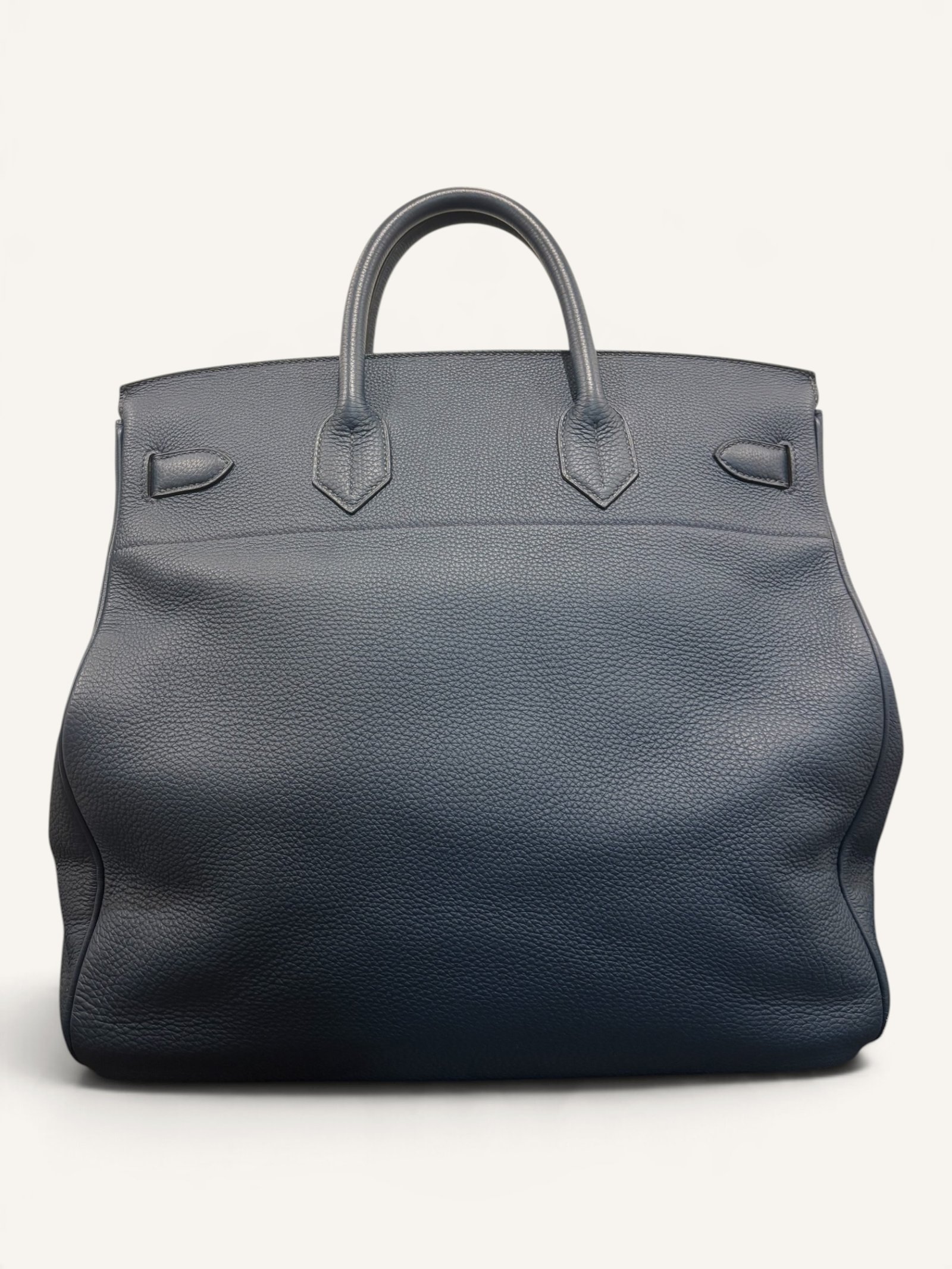 # Hermès HAC 40 Bleu de Prusse en cuir Togo, finitions Gold – 2015 Ce **HAC 40 Bleu de Prusse** en cuir Togo date de **2015**. Il se distingue par son magnifique bleu profond, associé à des **finitions Gold** qui apportent un contraste chaleureux. Présenté en **très bon état général**, cet exemplaire possède uniquement de légères traces d'utilisation au niveau des coins. Son format 40 et sa silhouette caractéristique lui confèrent une présence remarquable. **Dimensions : format 40 cm – dimensions complètes à compléter** **Matière : cuir Togo** **Couleur : Bleu de Prusse** **Finitions : Gold** **Année : 2015** **État : très bon état général, légères traces aux coins** Cette configuration associe l'élégance d'une couleur profonde à la texture du cuir Togo. Ainsi, le sac conserve une esthétique intemporelle tout en se distinguant des coloris plus traditionnels. --- ## HAC 40 Bleu de Prusse : une couleur profonde et élégante Le **Bleu de Prusse** fait partie des tonalités sombres particulièrement intéressantes de la palette Hermès. Sa profondeur lui donne une élégance proche de celle d'un bleu nuit. Cependant, ses nuances peuvent évoluer selon la lumière. Sous un éclairage naturel, le cuir peut révéler davantage de bleu. En revanche, dans une ambiance plus sombre, sa couleur apparaît plus intense. Cette richesse visuelle apporte une personnalité particulière au sac. De plus, le Bleu de Prusse s'associe facilement au noir, au gris, au beige et aux tons naturels. Il constitue donc une belle alternative aux grands sacs Hermès noirs ou marron. ## Le cuir Togo : une matière emblématique Le **cuir Togo** est apprécié pour son grain visible et son toucher souple. Il offre un équilibre intéressant entre structure et souplesse. Sur un grand format comme le HAC 40, cette matière permet de mettre en valeur les volumes du sac. Par ailleurs, sa surface grainée rend généralement les petites marques moins apparentes que sur certains cuirs lisses. Le résultat est un sac agréable à utiliser, tout en conservant une belle présence. Associé au Bleu de Prusse, le Togo révèle également de subtils jeux de lumière. ## Des finitions Gold au contraste raffiné Les **finitions Gold** jouent un rôle essentiel dans l'esthétique de cet exemplaire. Leur tonalité dorée contraste avec le bleu profond du cuir. Ainsi, les éléments métalliques deviennent de véritables détails décoratifs. Cette association apporte davantage de chaleur qu'une configuration accompagnée de finitions Palladium. De plus, le contraste entre le bleu et l'or renforce le caractère sophistiqué de ce HAC 40. Il s'agit d'une combinaison particulièrement élégante pour un grand sac de maroquinerie. ## Hermès HAC 40 : une silhouette historique Le **HAC**, ou *Haut à Courroies*, occupe une place particulière dans l'histoire d'Hermès. Créé à la fin du XIXe siècle, il était initialement destiné au transport des équipements équestres. Son nom fait référence à sa silhouette haute et à son système de fermeture à courroies. Au fil du temps, le modèle a évolué pour devenir une pièce emblématique de la maroquinerie de voyage Hermès. Aujourd'hui, il séduit aussi bien les collectionneurs que les amateurs de grands sacs de luxe. Son format généreux et sa structure reconnaissable lui donnent une identité distincte du Birkin. ## Un HAC 40 datant de 2015 Cet exemplaire a été fabriqué en **2015**. Il possède donc plus de dix années d'ancienneté. Malgré son âge, il est conservé dans un **très bon état général**. Seules de légères traces sont visibles au niveau des coins. Ces marques correspondent à une utilisation normale et restent limitées. Par ailleurs, elles sont clairement présentées afin de permettre une acquisition en toute transparence. ## Très bon état avec de légères traces aux coins L'état de conservation constitue un critère essentiel pour un sac Hermès d'occasion. Ce **HAC 40 Bleu de Prusse** est proposé en très bon état général. Le cuir Togo conserve une belle présentation. Cependant, quelques légères marques sont présentes aux coins. Ces zones sont naturellement exposées aux frottements lors de l'utilisation d'un sac. Nos photographies détaillées permettent donc d'apprécier précisément leur importance. Ainsi, l'acheteur dispose d'une description fidèle de l'état réel de la pièce. ## Le format HAC 40 : volume et élégance Le **format 40** offre un volume généreux. Il permet de transporter facilement de nombreux effets personnels. Ce sac peut notamment accueillir : - Un portefeuille. - Un téléphone. - Des lunettes. - Une pochette. - Des documents. - Une tablette. - Divers accessoires personnels. De plus, sa silhouette haute lui donne une présence plus affirmée que celle d'un sac à main classique. Il peut donc être envisagé comme un grand sac quotidien ou un élégant compagnon de déplacement. ## Un grand sac Hermès au caractère affirmé Le HAC 40 possède une esthétique immédiatement reconnaissable. Sa silhouette structurée et ses proportions généreuses lui confèrent une allure particulière. Sur cet exemplaire, le cuir Togo Bleu de Prusse apporte davantage de souplesse visuelle. En parallèle, les finitions Gold soulignent les lignes du sac. Ainsi, l'ensemble reste élégant malgré son volume important. Cette combinaison conviendra particulièrement aux amateurs de pièces Hermès discrètes par leur couleur, mais remarquables par leur format. ## Pourquoi choisir un HAC 40 Bleu de Prusse ? Cet exemplaire réunit plusieurs caractéristiques intéressantes : - **Modèle :** Hermès Haut à Courroies 40. - **Année :** 2015. - **Matière :** cuir Togo. - **Couleur :** Bleu de Prusse. - **Finitions :** Gold. - **État :** très bon état général. - **À noter :** légères traces d'utilisation aux coins. - **Format :** 40 cm. Cette configuration se distingue notamment par son équilibre entre couleur profonde, cuir grainé et finitions dorées. Elle constitue donc une belle option pour enrichir une collection Hermès ou acquérir un grand sac élégant. ## Une alternative aux HAC noirs et marron Les grands sacs Hermès sont souvent recherchés dans des couleurs classiques. Le noir, le Gold ou l'Ébène restent naturellement des choix intemporels. Toutefois, le Bleu de Prusse permet d'apporter davantage de personnalité sans choisir une couleur trop vive. Son intensité reste discrète. De plus, les finitions Gold créent un contraste qui souligne parfaitement le bleu du cuir. Ainsi, ce HAC 40 constitue une alternative particulièrement intéressante aux configurations traditionnelles. ## Un sac Hermès à porter et à conserver Grâce à son cuir Togo et à son format généreux, cet exemplaire peut être utilisé régulièrement. Il peut accompagner un vestiaire élégant ou plus décontracté. Cependant, sa couleur particulière lui donne également un intérêt pour les amateurs de configurations Hermès moins courantes. Le Bleu de Prusse permet notamment de varier une collection composée de sacs noirs, marron ou beiges. Ce HAC 40 peut donc aussi bien devenir un sac personnel qu'une belle pièce de collection. ## Pourquoi acheter votre HAC Hermès chez The Vintage Traveler ? Chez **The Vintage Traveler**, nous sélectionnons des sacs Hermès vintage et d'occasion pour leur authenticité, leur qualité et leurs caractéristiques. Chaque pièce est examinée avec attention afin de présenter précisément son état et ses particularités. ### Nos garanties ✔ **Magasin physique situé au Marché Paul Bert Serpette**, au cœur des Puces de Saint-Ouen. ✔ Sac **expertisé et certifié authentique** par un spécialiste du luxe vintage et d'occasion. ✔ Certificat d'authenticité fourni avec votre achat. ✔ Photographies détaillées et fidèles à l'état réel du sac. ✔ Description transparente des légères traces présentes aux coins. ✔ Accompagnement personnalisé avant et après votre achat. ✔ Expédition internationale rapide, sécurisée et assurée. --- ## Caractéristiques du Hermès HAC 40 **Maison :** Hermès **Modèle :** Haut à Courroies – HAC 40 **Année :** 2015 **Matière :** Cuir Togo **Couleur :** Bleu de Prusse **Finitions :** Gold **Format :** 40 cm **Dimensions complètes :** à compléter **État :** Très bon état général **À noter :** Légères traces d'utilisation aux coins --- ## Un élégant HAC 40 Bleu de Prusse de 2015 Ce **HAC 40 Bleu de Prusse** en cuir Togo constitue une superbe interprétation du célèbre Haut à Courroies Hermès. Sa couleur profonde, associée aux **finitions Gold**, lui donne une esthétique particulièrement raffinée. Datant de **2015**, cet exemplaire est conservé dans un **très bon état général**, avec seulement de légères traces aux coins. Enfin, son format 40 offre un volume généreux tout en conservant la silhouette emblématique du HAC. Une belle pièce pour les amateurs de **sacs Hermès d'occasion**, de grands formats et de couleurs sophistiquées.