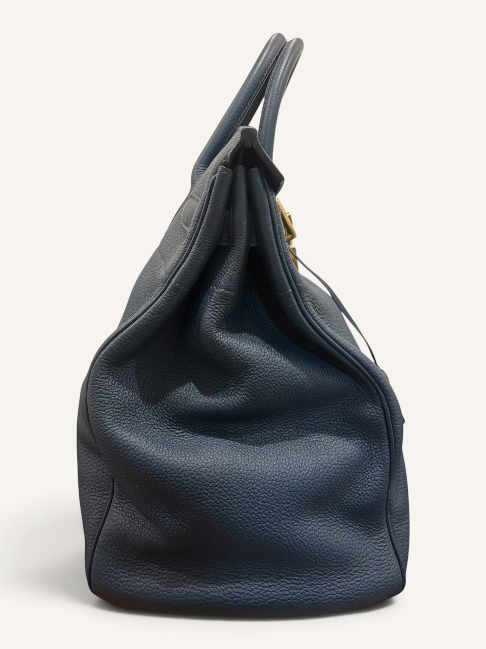 # Hermès HAC 40 Bleu de Prusse en cuir Togo, finitions Gold – 2015 Ce **HAC 40 Bleu de Prusse** en cuir Togo date de **2015**. Il se distingue par son magnifique bleu profond, associé à des **finitions Gold** qui apportent un contraste chaleureux. Présenté en **très bon état général**, cet exemplaire possède uniquement de légères traces d'utilisation au niveau des coins. Son format 40 et sa silhouette caractéristique lui confèrent une présence remarquable. **Dimensions : format 40 cm – dimensions complètes à compléter** **Matière : cuir Togo** **Couleur : Bleu de Prusse** **Finitions : Gold** **Année : 2015** **État : très bon état général, légères traces aux coins** Cette configuration associe l'élégance d'une couleur profonde à la texture du cuir Togo. Ainsi, le sac conserve une esthétique intemporelle tout en se distinguant des coloris plus traditionnels. --- ## HAC 40 Bleu de Prusse : une couleur profonde et élégante Le **Bleu de Prusse** fait partie des tonalités sombres particulièrement intéressantes de la palette Hermès. Sa profondeur lui donne une élégance proche de celle d'un bleu nuit. Cependant, ses nuances peuvent évoluer selon la lumière. Sous un éclairage naturel, le cuir peut révéler davantage de bleu. En revanche, dans une ambiance plus sombre, sa couleur apparaît plus intense. Cette richesse visuelle apporte une personnalité particulière au sac. De plus, le Bleu de Prusse s'associe facilement au noir, au gris, au beige et aux tons naturels. Il constitue donc une belle alternative aux grands sacs Hermès noirs ou marron. ## Le cuir Togo : une matière emblématique Le **cuir Togo** est apprécié pour son grain visible et son toucher souple. Il offre un équilibre intéressant entre structure et souplesse. Sur un grand format comme le HAC 40, cette matière permet de mettre en valeur les volumes du sac. Par ailleurs, sa surface grainée rend généralement les petites marques moins apparentes que sur certains cuirs lisses. Le résultat est un sac agréable à utiliser, tout en conservant une belle présence. Associé au Bleu de Prusse, le Togo révèle également de subtils jeux de lumière. ## Des finitions Gold au contraste raffiné Les **finitions Gold** jouent un rôle essentiel dans l'esthétique de cet exemplaire. Leur tonalité dorée contraste avec le bleu profond du cuir. Ainsi, les éléments métalliques deviennent de véritables détails décoratifs. Cette association apporte davantage de chaleur qu'une configuration accompagnée de finitions Palladium. De plus, le contraste entre le bleu et l'or renforce le caractère sophistiqué de ce HAC 40. Il s'agit d'une combinaison particulièrement élégante pour un grand sac de maroquinerie. ## Hermès HAC 40 : une silhouette historique Le **HAC**, ou *Haut à Courroies*, occupe une place particulière dans l'histoire d'Hermès. Créé à la fin du XIXe siècle, il était initialement destiné au transport des équipements équestres. Son nom fait référence à sa silhouette haute et à son système de fermeture à courroies. Au fil du temps, le modèle a évolué pour devenir une pièce emblématique de la maroquinerie de voyage Hermès. Aujourd'hui, il séduit aussi bien les collectionneurs que les amateurs de grands sacs de luxe. Son format généreux et sa structure reconnaissable lui donnent une identité distincte du Birkin. ## Un HAC 40 datant de 2015 Cet exemplaire a été fabriqué en **2015**. Il possède donc plus de dix années d'ancienneté. Malgré son âge, il est conservé dans un **très bon état général**. Seules de légères traces sont visibles au niveau des coins. Ces marques correspondent à une utilisation normale et restent limitées. Par ailleurs, elles sont clairement présentées afin de permettre une acquisition en toute transparence. ## Très bon état avec de légères traces aux coins L'état de conservation constitue un critère essentiel pour un sac Hermès d'occasion. Ce **HAC 40 Bleu de Prusse** est proposé en très bon état général. Le cuir Togo conserve une belle présentation. Cependant, quelques légères marques sont présentes aux coins. Ces zones sont naturellement exposées aux frottements lors de l'utilisation d'un sac. Nos photographies détaillées permettent donc d'apprécier précisément leur importance. Ainsi, l'acheteur dispose d'une description fidèle de l'état réel de la pièce. ## Le format HAC 40 : volume et élégance Le **format 40** offre un volume généreux. Il permet de transporter facilement de nombreux effets personnels. Ce sac peut notamment accueillir : - Un portefeuille. - Un téléphone. - Des lunettes. - Une pochette. - Des documents. - Une tablette. - Divers accessoires personnels. De plus, sa silhouette haute lui donne une présence plus affirmée que celle d'un sac à main classique. Il peut donc être envisagé comme un grand sac quotidien ou un élégant compagnon de déplacement. ## Un grand sac Hermès au caractère affirmé Le HAC 40 possède une esthétique immédiatement reconnaissable. Sa silhouette structurée et ses proportions généreuses lui confèrent une allure particulière. Sur cet exemplaire, le cuir Togo Bleu de Prusse apporte davantage de souplesse visuelle. En parallèle, les finitions Gold soulignent les lignes du sac. Ainsi, l'ensemble reste élégant malgré son volume important. Cette combinaison conviendra particulièrement aux amateurs de pièces Hermès discrètes par leur couleur, mais remarquables par leur format. ## Pourquoi choisir un HAC 40 Bleu de Prusse ? Cet exemplaire réunit plusieurs caractéristiques intéressantes : - **Modèle :** Hermès Haut à Courroies 40. - **Année :** 2015. - **Matière :** cuir Togo. - **Couleur :** Bleu de Prusse. - **Finitions :** Gold. - **État :** très bon état général. - **À noter :** légères traces d'utilisation aux coins. - **Format :** 40 cm. Cette configuration se distingue notamment par son équilibre entre couleur profonde, cuir grainé et finitions dorées. Elle constitue donc une belle option pour enrichir une collection Hermès ou acquérir un grand sac élégant. ## Une alternative aux HAC noirs et marron Les grands sacs Hermès sont souvent recherchés dans des couleurs classiques. Le noir, le Gold ou l'Ébène restent naturellement des choix intemporels. Toutefois, le Bleu de Prusse permet d'apporter davantage de personnalité sans choisir une couleur trop vive. Son intensité reste discrète. De plus, les finitions Gold créent un contraste qui souligne parfaitement le bleu du cuir. Ainsi, ce HAC 40 constitue une alternative particulièrement intéressante aux configurations traditionnelles. ## Un sac Hermès à porter et à conserver Grâce à son cuir Togo et à son format généreux, cet exemplaire peut être utilisé régulièrement. Il peut accompagner un vestiaire élégant ou plus décontracté. Cependant, sa couleur particulière lui donne également un intérêt pour les amateurs de configurations Hermès moins courantes. Le Bleu de Prusse permet notamment de varier une collection composée de sacs noirs, marron ou beiges. Ce HAC 40 peut donc aussi bien devenir un sac personnel qu'une belle pièce de collection. ## Pourquoi acheter votre HAC Hermès chez The Vintage Traveler ? Chez **The Vintage Traveler**, nous sélectionnons des sacs Hermès vintage et d'occasion pour leur authenticité, leur qualité et leurs caractéristiques. Chaque pièce est examinée avec attention afin de présenter précisément son état et ses particularités. ### Nos garanties ✔ **Magasin physique situé au Marché Paul Bert Serpette**, au cœur des Puces de Saint-Ouen. ✔ Sac **expertisé et certifié authentique** par un spécialiste du luxe vintage et d'occasion. ✔ Certificat d'authenticité fourni avec votre achat. ✔ Photographies détaillées et fidèles à l'état réel du sac. ✔ Description transparente des légères traces présentes aux coins. ✔ Accompagnement personnalisé avant et après votre achat. ✔ Expédition internationale rapide, sécurisée et assurée. --- ## Caractéristiques du Hermès HAC 40 **Maison :** Hermès **Modèle :** Haut à Courroies – HAC 40 **Année :** 2015 **Matière :** Cuir Togo **Couleur :** Bleu de Prusse **Finitions :** Gold **Format :** 40 cm **Dimensions complètes :** à compléter **État :** Très bon état général **À noter :** Légères traces d'utilisation aux coins --- ## Un élégant HAC 40 Bleu de Prusse de 2015 Ce **HAC 40 Bleu de Prusse** en cuir Togo constitue une superbe interprétation du célèbre Haut à Courroies Hermès. Sa couleur profonde, associée aux **finitions Gold**, lui donne une esthétique particulièrement raffinée. Datant de **2015**, cet exemplaire est conservé dans un **très bon état général**, avec seulement de légères traces aux coins. Enfin, son format 40 offre un volume généreux tout en conservant la silhouette emblématique du HAC. Une belle pièce pour les amateurs de **sacs Hermès d'occasion**, de grands formats et de couleurs sophistiquées.